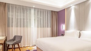 Ein Hotelzimmer mit einem großen Bett, einem Schreibtisch, einem Stuhl und einem Fenster mit leichtem Vorhang.