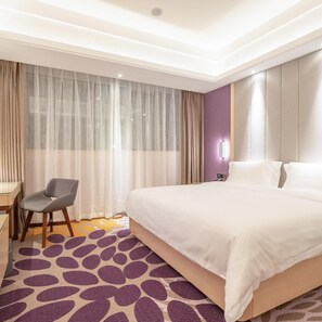 Habitación de hotel con una cama grande, un escritorio, una silla y una ventana con cortinas translúcidas.