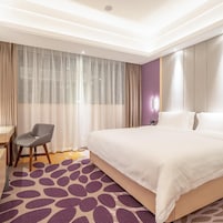 Habitación de hotel con una cama grande, un escritorio, una silla y una ventana con cortinas translúcidas.