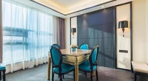 Habitació d'hotel amb taula de menjador, quatre cadires, finestra gran amb cortines i porta corredissa.