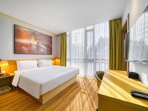 Ein Hotelzimmer mit einem gro ßen Bett, einem Schreibtisch, einem Stuhl, einem Fernseher und einem Fenster mit Vorhängen.