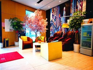 A modern lobby with seating areas, a large artificial tree, and a colorful mural on the wall. - IU Hotel (Suzhou)