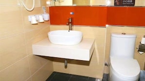 Casa de banho com lavatório branco, sanita e secador de cabelo na parede.