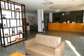 Un área de recepción con un sofá color beige, una estantería de madera y un mostrador de recepción.