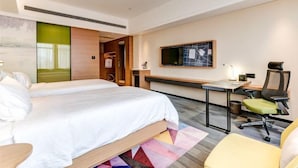 Una habitación de hotel con cama, escritorio, silla y televisor en la pared.
