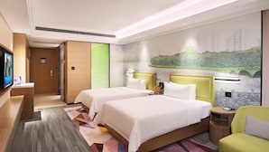 Habitación de hotel con dos camas, televisor, escritorio y una pared con un mural de un paisaje urbano.
