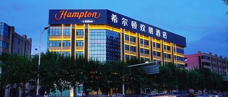 Un hotel con un llamativo letrero de 'Hampton by Hilton', varios pisos y un diseño arquitectónico moderno.