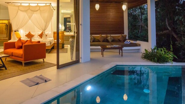 Ein modernes Haus mit Swimmingpool, einem Wohnbereich inklusive Sofa und Couchtisch sowie einem Schlafzimmer mit Bett und Vorhängen.