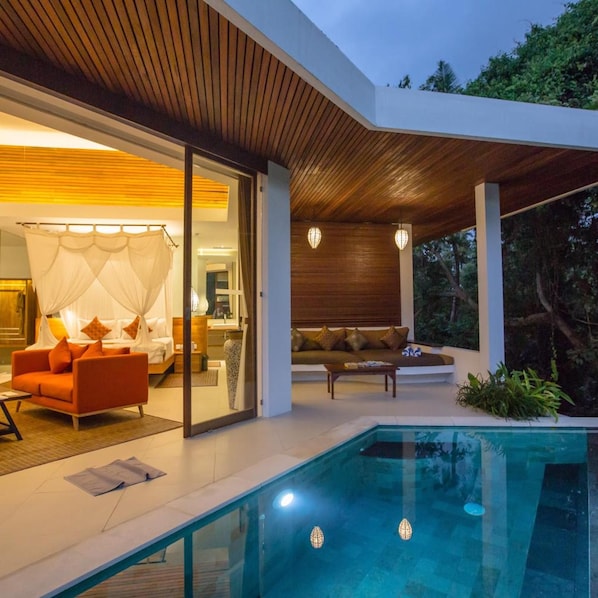 Et moderne hus med swimmingpool, opholdsstue med sofa og sofabord, samt et soveværelse med seng og gardiner.