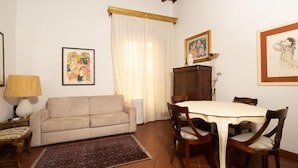 Ein Wohnzimmer mit einer Couch, einem Esstisch mit Stühlen, einem gemusterten Teppich und Kunstwerken an den Wänden.
