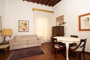 A living room with a sofa, a dining table with chairs, a patterned rug, and artwork on the walls. - Bardi Suite (Florence)