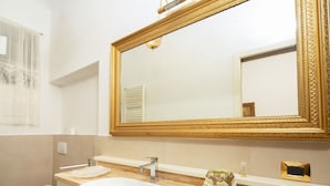 Ein Badezimmer mit einem weißen Waschbecken, einem spiegel mit goldener Rahmen, einer Toilette und einem Waschtisch mit einer Seifenspender.