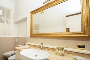 A bathroom with a white sink, a gold-framed mirror, a toilet, and a vanity with a soap dispenser. - Bardi Suite (Florence)
