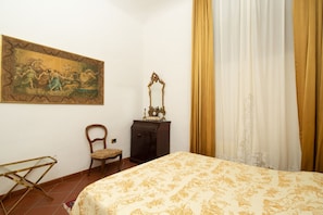 A bedroom with a bed, a chair, a dresser, a mirror, and a painting on the wall. - Bardi Suite (Florence)