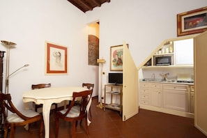 A dining area with a table and chairs, a television, and a kitchen area with cabinets and a microwave. - Bardi Suite (Florence)