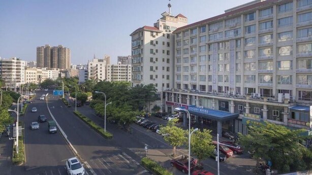 A multi-story hotel with a parking lot in front, surrounded by other buildings. - Echarm Hotel (Haikou)