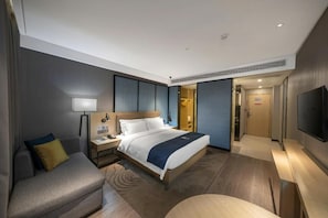 Habitación de hotel moderna con cama, mesita de noche, lámpara y televisor de pantalla plana.