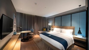 A hotel room with a large bed, a desk with a chair, a television, and a window with curtains. - Echarm Hotel (Haikou)