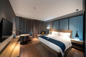 Una habitación de hotel con una cama grande, un escritorio con una silla, televisión y una ventana con cortinas.