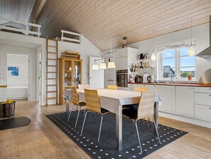 A modern kitchen with wooden cabinets, a dining table, and pendant lights. - "Gunda" - 150m from the sea by Interhome (Nysted)