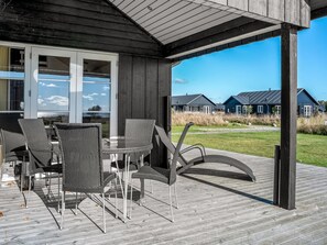 A covered outdoor area with a table and chairs, a wooden deck, and a view of houses in the background. - "Gunda" - 150m from the sea by Interhome (Nysted)
