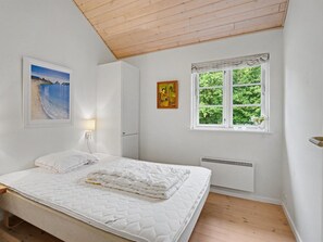 Un dormitorio con cama, ventana con vistas a árboles, un cuadro en la pared y un radiador.