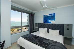 A bedroom with a large bed, a ceiling fan, a view of the sea, and a painting on the wall. - False Bay Inn (Cape Town)
