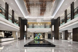 Eine großzügige Lobby mit spiegelndem Boden, einem Empfangstresen und einer zentralen Zierwasseranlage.