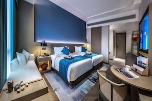 Ein modernes Hotelzimmer mit zwei Betten, einer Couch, einem Schreibtisch und einem Fernseher.