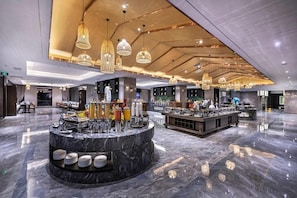 Eine großzügige Lobby mit Marmorboden, einer zentralen Bar und mehreren Hängeleuchten.