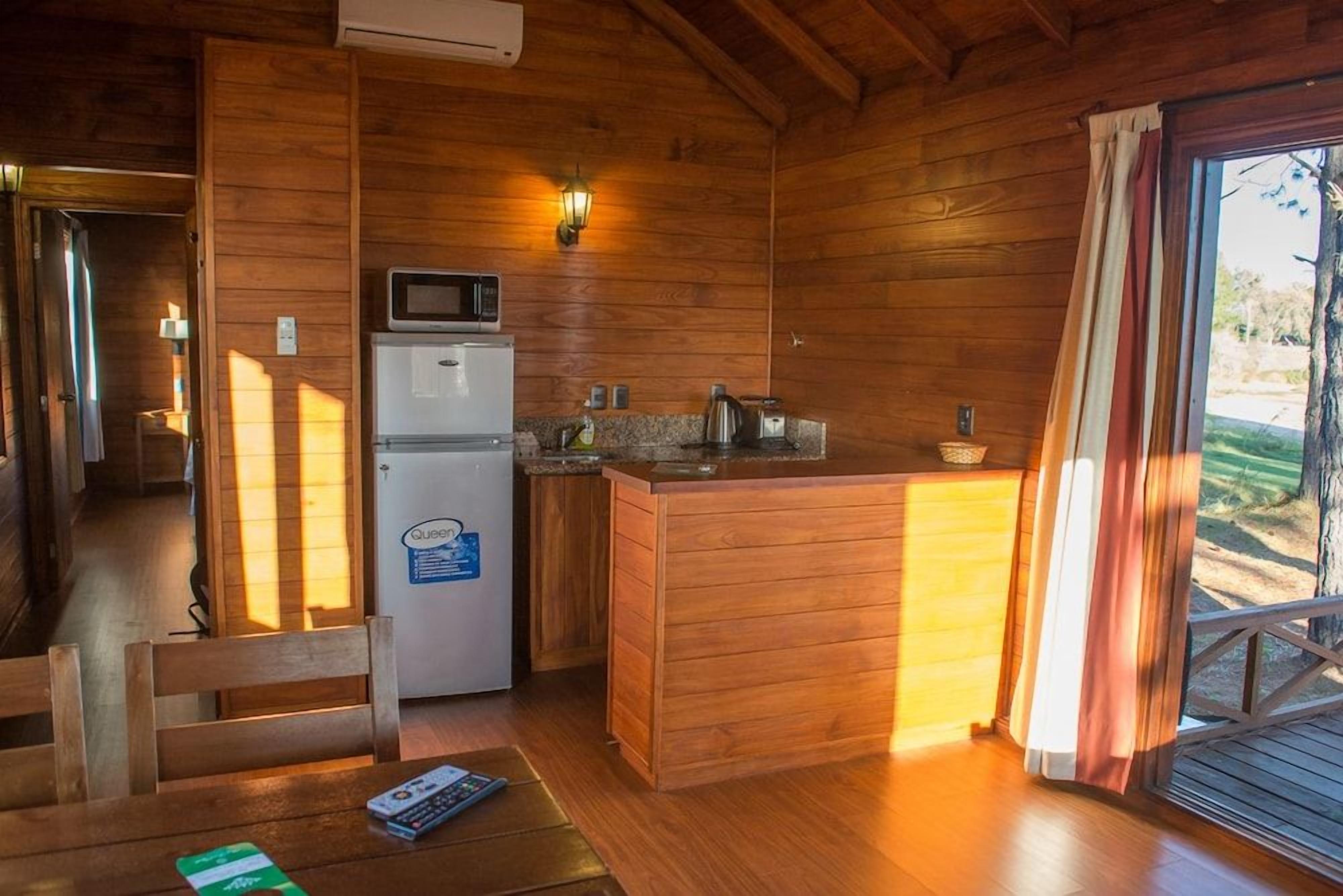 Une cuisine compacte aux murs en bois, équipée d’un réfrigérateur, d’un four à micro-ondes et d’un petit îlot central.