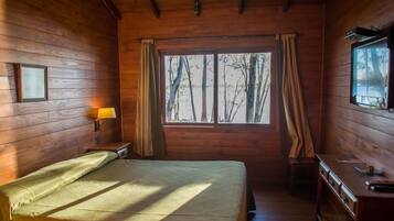 A wooden cabin room with a bed, a desk, and a window with curtains.