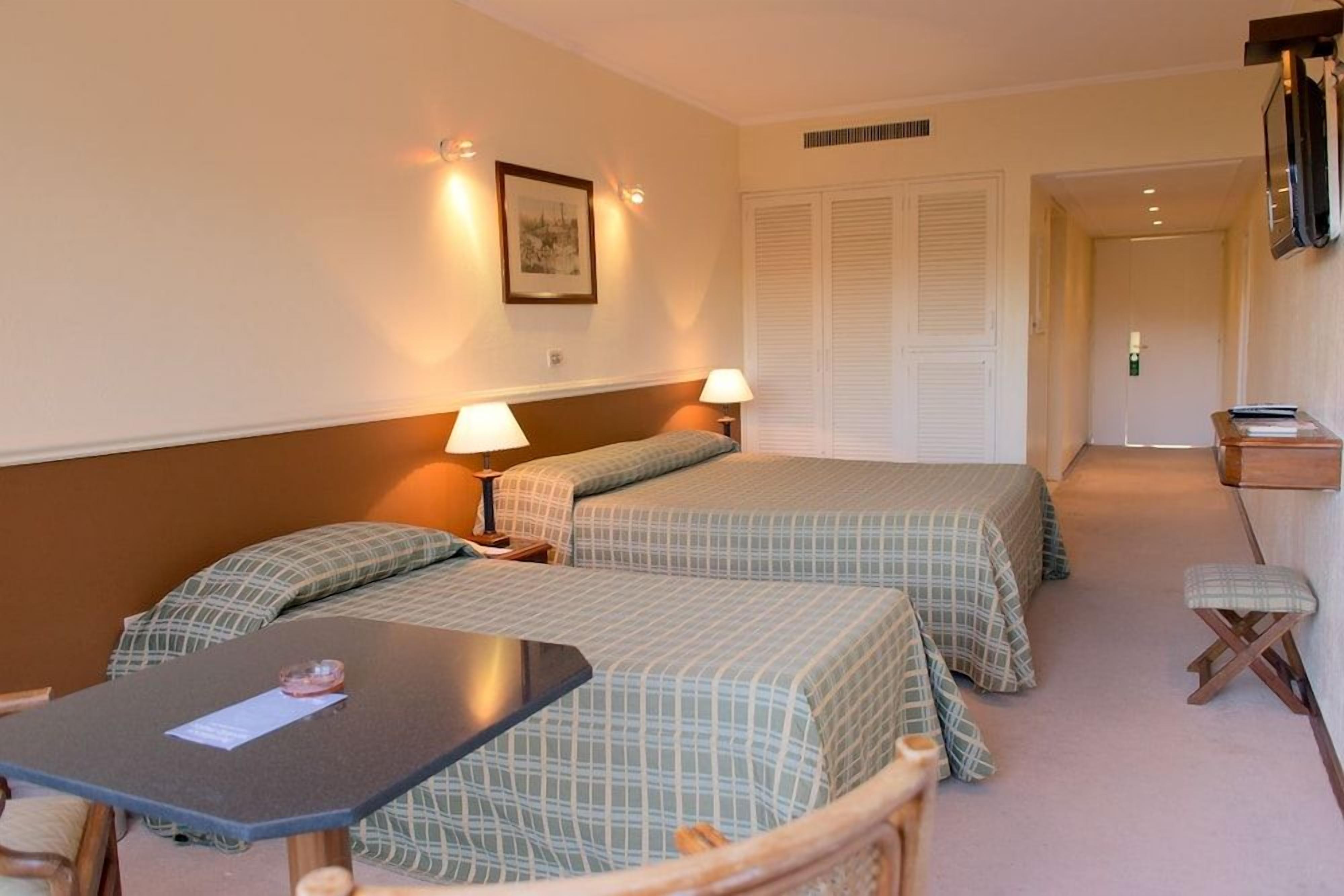 A hotel room with two beds, a small table, a chair, a TV, and a picture on the wall.