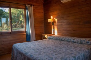 A room with a bed, a nightstand, a lamp, and a window with curtains.