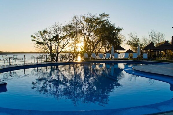 A swimming pool with a sunset view, surrounded by lounge chairs and umbrellas. - Hotel Horacio Quiroga (Salto)
