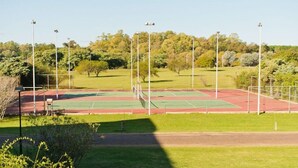 Een buitenbaan voor tennis met omliggend groen en een heldere lucht.