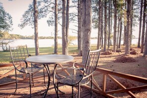 An outdoor seating area with a round table and metal chairs, surrounded by trees and a view of a lake.