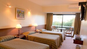 Een hotelkamer met twee bedden, een bureau, een stoel en een raam met gordijnen.