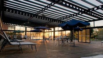 An outdoor patio with lounge chairs and umbrellas, a covered seating area, and a view of the sunset.