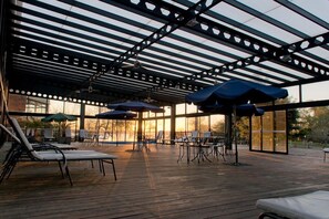 Un patio exterior con sillones de descanso y sombrillas, una zona de estar cubierta y vistas al atardecer.