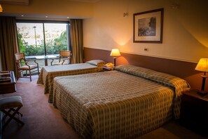Habitación de hotel con dos camas, un escritorio, una silla, una lámpara y una ventana con cortinas.