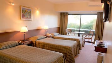 A hotel room with two beds, a small table, a chair, and a window with curtains.