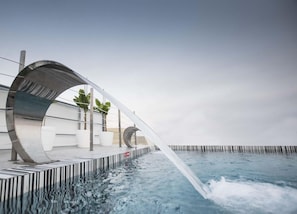 Un área de piscina moderna con una estructura curva, plantas en macetas y una vista despejada del agua.