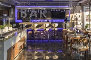 Zona de bar con diseño moderno, que incluye barra, taburetes y un área de estar con mesas y sillas.