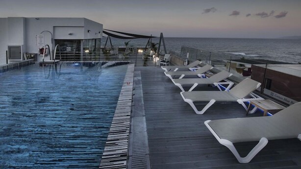 Ein Pool ohne Ende mit Liegestühlen und Blick auf das Meer.