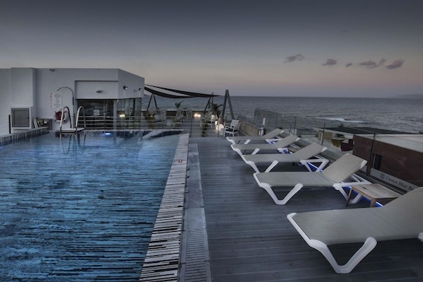 Une piscine à débordement avec des chaises longues et une vue sur la mer.