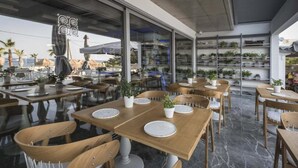 Ein Außenbereich zum Essen mit Holztischen und -stühlen, Blumentöpfen und Blick auf den Strand.