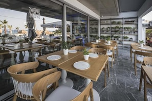 Un espace extérieur aménagé pour les repas, avec des tables et des chaises en bois, des plantes en pot et une vue sur la plage.