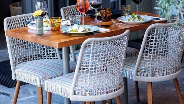 Un espace extérieur aménagé pour les repas, avec des chaises en osier et une table en bois, le tout préparé pour deux personnes.