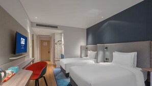 Ein Hotelzimmer mit zwei Betten, einem Schreibtisch mit Stuhl, einem Fernseher und einem Badezimmer mit Dusche.